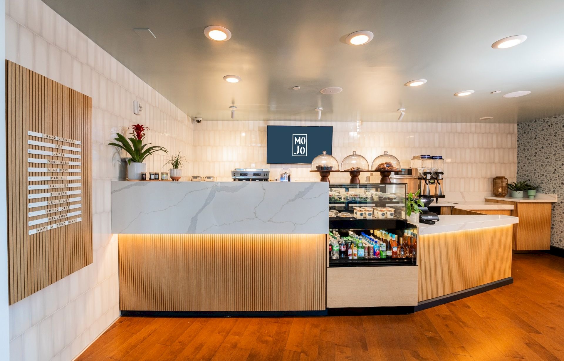 A modern cafe counter with a marble top, warm wood accents, display case, and ambient lighting. Looks clean and inviting to order coffee or pastries.