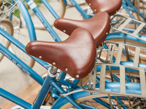 A row of blue bicycles with brown saddles and baskets, parked together in a bike-share setup, money visible around them.