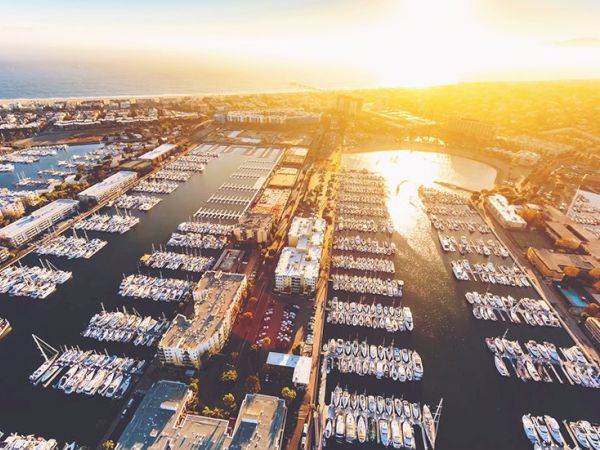 Aerial view of a marina at sunset, with rows of boats docked in calm waters and illuminated by golden light.