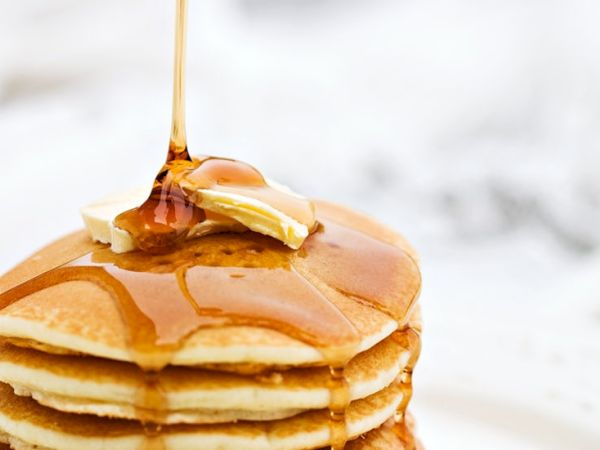 Stack of fluffy pancakes drizzled with syrup and a pat of butter slowly melting on top, glossy drizzle cascading down the sides.