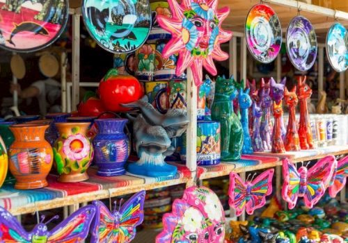 Colorful carnival souvenirs: wind chimes, masks, vases, butterfly wings, sun shapes, and festive figurines on display at a market booth.