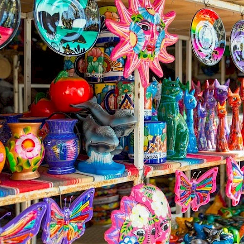 Colorful carnival souvenirs: wind chimes, masks, vases, butterfly wings, sun shapes, and festive figurines on display at a market booth.