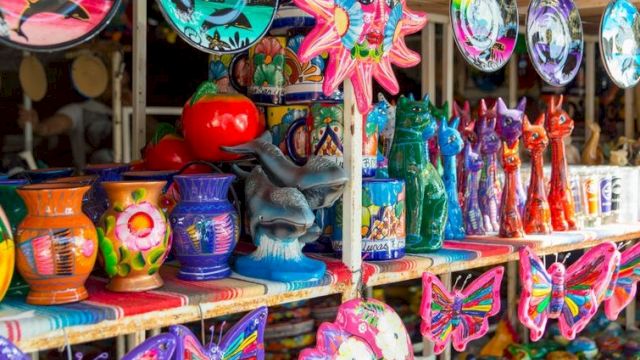 Colorful carnival souvenirs: wind chimes, masks, vases, butterfly wings, sun shapes, and festive figurines on display at a market booth.