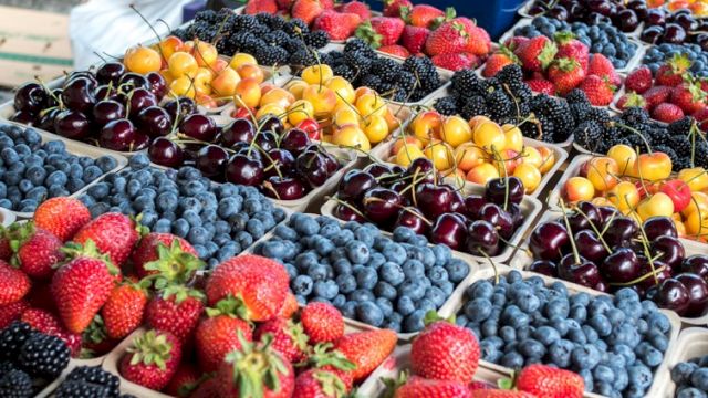 Colorful berries and stone fruits arranged in neat crates at a market, with ripe strawberries, blueberries, cherries, and apricots. Top it at 140 characters, always ending the sentence.