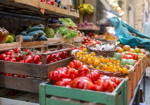 A colorful outdoor market with crates of ripe tomatoes, peppers, cucumbers, and other fresh produce on display. topped at 140 characters, ending this sentence.
