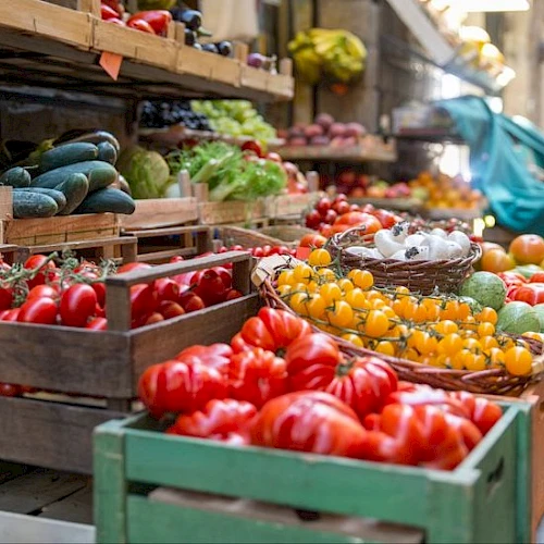 A colorful outdoor market with crates of ripe tomatoes, peppers, cucumbers, and other fresh produce on display. topped at 140 characters, ending this sentence.