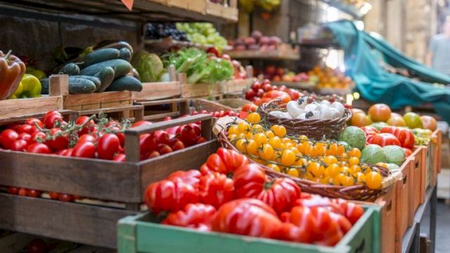 A colorful outdoor market with crates of ripe tomatoes, peppers, cucumbers, and other fresh produce on display. topped at 140 characters, ending this sentence.
