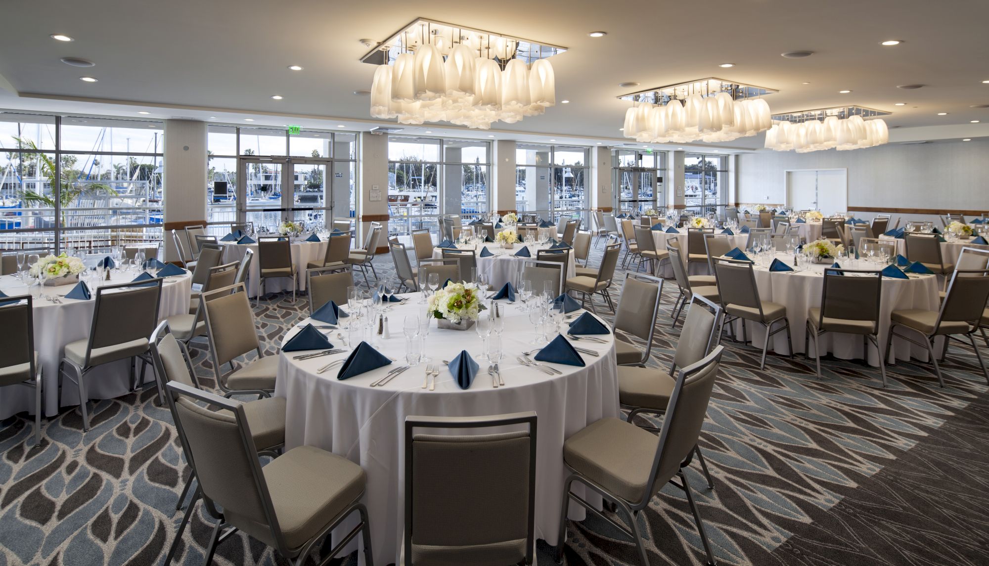 A banquet hall set for a formal event with round tables, chairs, white tablecloths, menu cards, and flower centerpieces, ready to host guests.