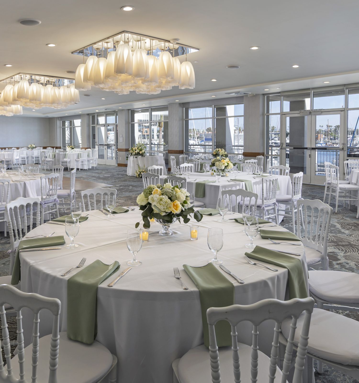 Elegant banquet hall with round tables, white chairs, pastel green napkins, and soft floral centerpieces for a formal event.