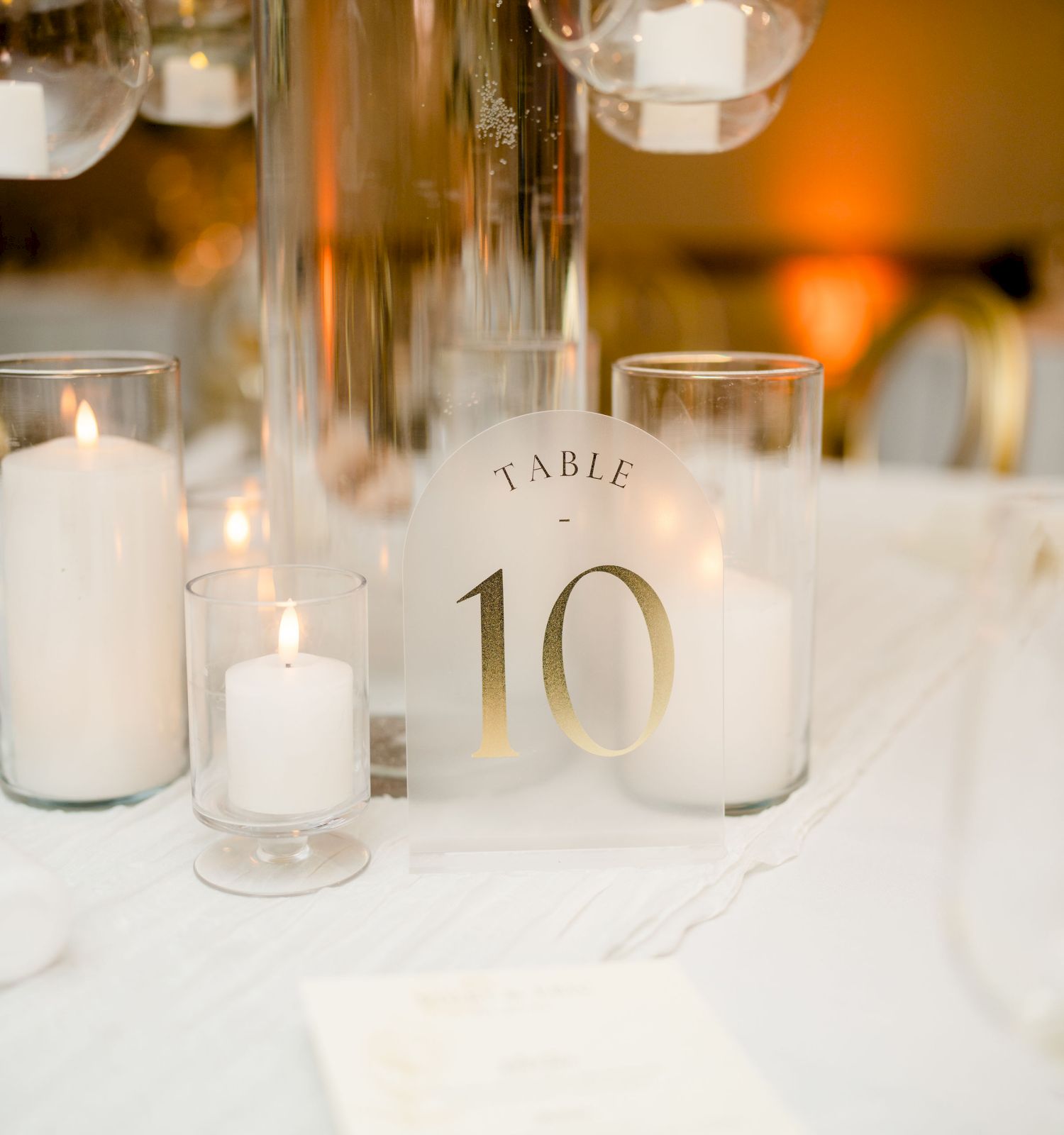 A candlelit banquet table with a glass centerpiece, lit candles, and a &ldquo;Table 10&rdquo; sign in a warm, elegant setting.