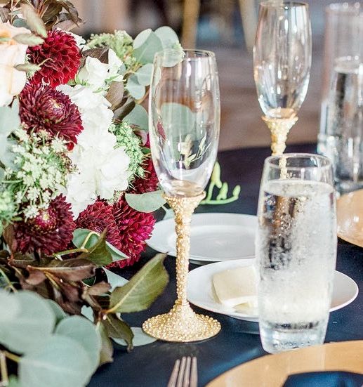 Elegant place setting with glassware, a floral centerpiece, and navy tablecloth accents, suggesting a formal event.