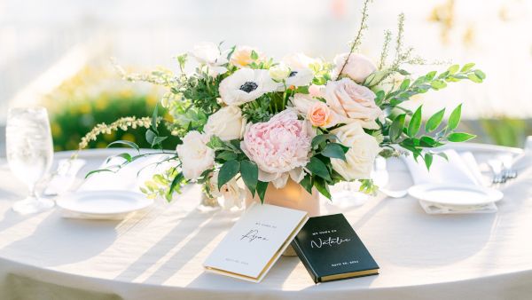 A elegant table setup with a lush floral centerpiece, white and pastel flowers, place settings, and two menu cards on a sunlit table.