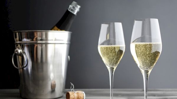 Two champagne flutes of bubbly with an ice bucket holding a bottle and a cork on the side, ready for a celebratory toast.