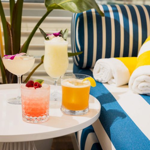 A colorful tea break with striped cushions, small yellow chair, orange juice, pastries, and a teapot on a table.