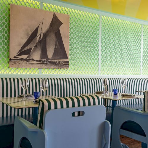 A vibrant indoor scene with green and purple lighting, wall art, and a row of colorful seats or booths along a curved counter.