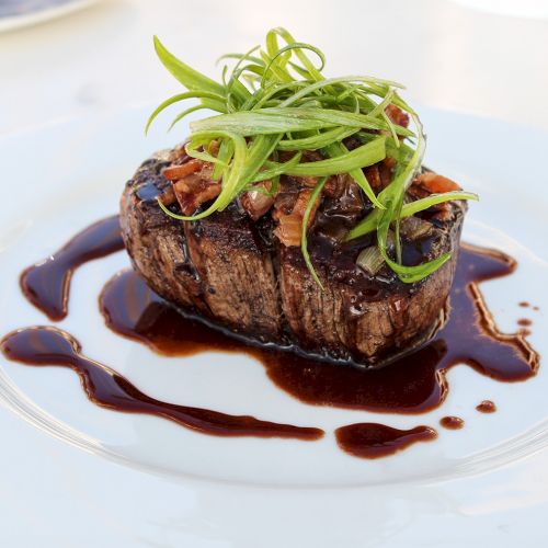 A perfectly seared steak topped with microgreens on a glossy sauce, plated elegantly with a decorative drizzle around it.