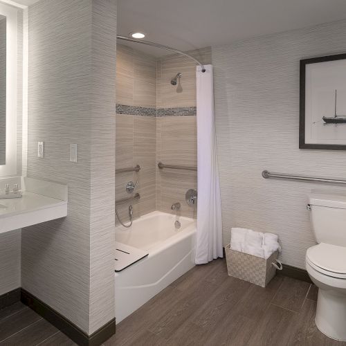 A modern bathroom with a glass-enclosed shower, white tile walls, a wall-mounted sink, a mirror, and a towel bar; warm, minimal decor.