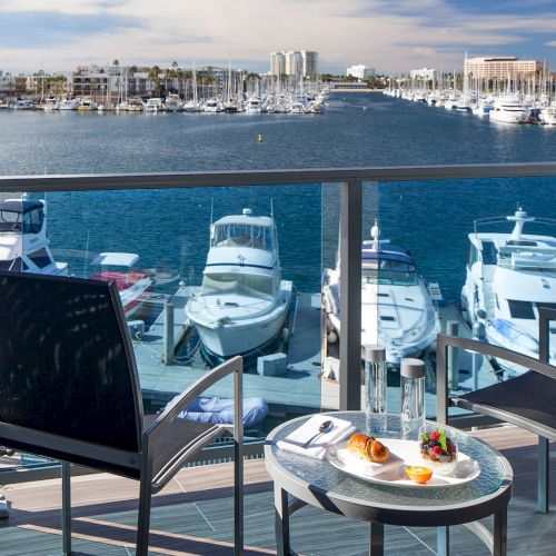 A seaside restaurant table on a balcony overlooking a marina with boats, water, and a scenic coastal view.
