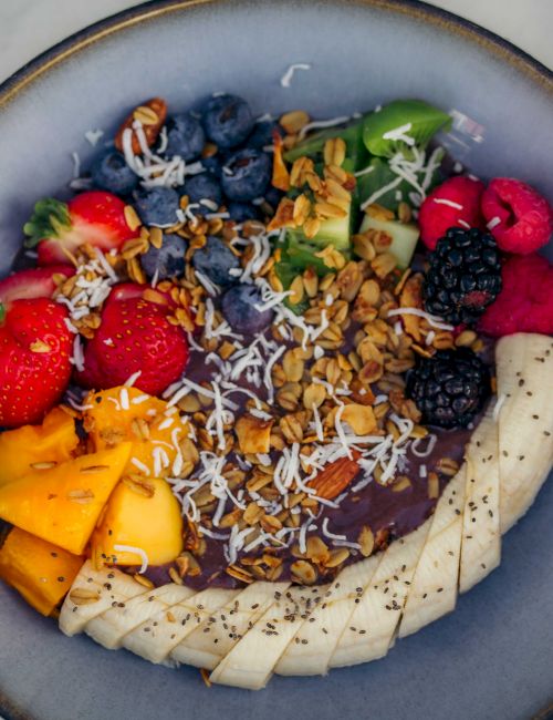 A vibrant smoothie bowl topped with mango, banana, berries, granola, coconut flakes, and nuts, arranged in a colorful, healthy swirl.