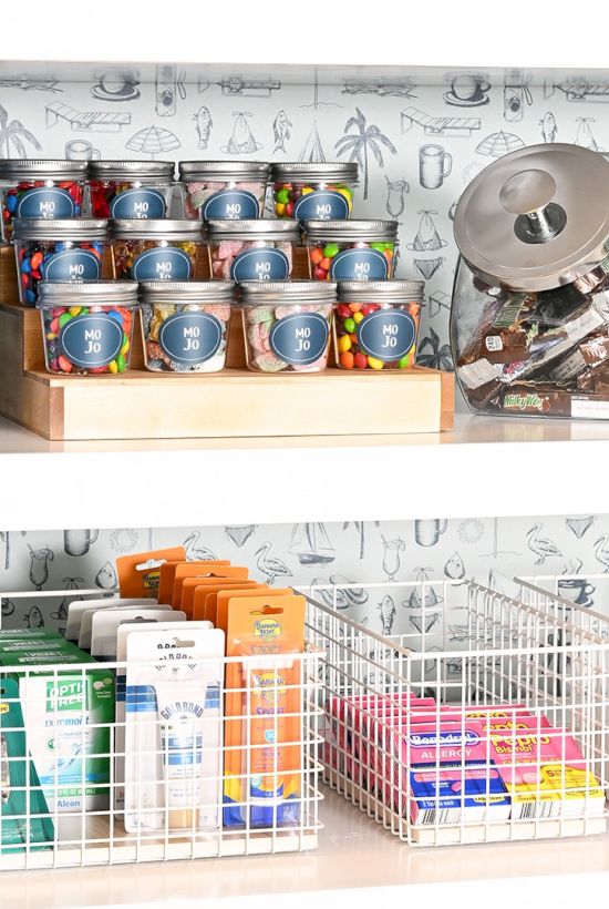 A store shelf with canned drinks, blue MJD containers, and metal wire baskets holding boxed and bottled items, plus a circular electronics item on the top shelf.