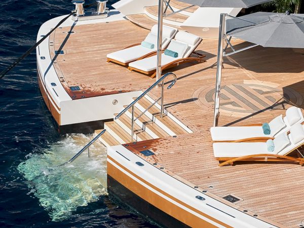 Aerial view of a wooden deck yacht with sun loungers, umbrellas, and steps into the water, anchored by the sea.