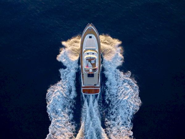 Aerial view of a small motorboat speeding through dark blue water, leaving white foamy wake behind as it moves forward.